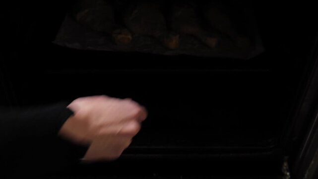 Hand putting a baking tray with raw marinated chicken drumsticks into a preheated oven. Start of the roasting process at home. Close-up of home cooking process