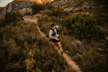 Endurance athlete running along a narrow trail through rugged mountain terrain surrounded by wild vegetation and rocky landscape. Outdoor training session focused on stamina, endurance and performance © aitor