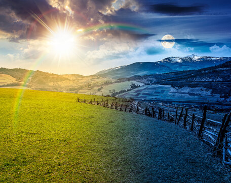 Spring equinox rural landscape. day meet night. sun and moon over Wooden fence along the path through agricultural fields in mountains. countryside scenery under cloudy sky. remote alpine pasture