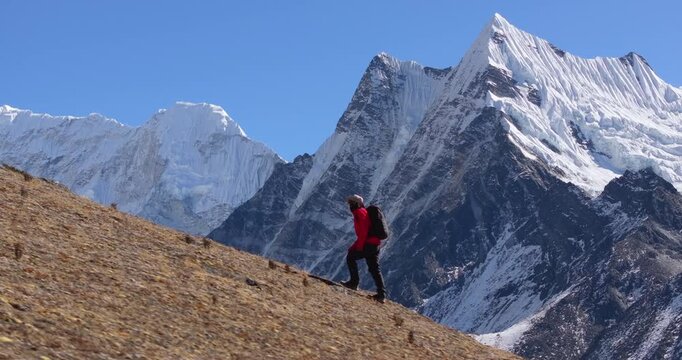 A solo trekker hiking along the Manaslu Circuit Trail in Nepal with dramatic snow-capped Himalayan mountain range rising in the background.