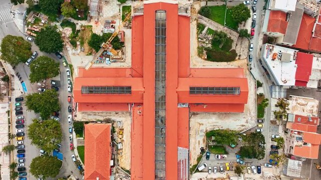 Aerial view of the vibrant Platia Agoras Market Hall with its red roof contrasting against the greenery and surrounding architecture, Chania, Chania, Greece.