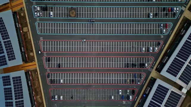Aerial view of rows of parked cars in a parking lot, bordered by buildings with solar panels, creating a geometric pattern of energy and transport, Karuizawa, Nagano, Japan.