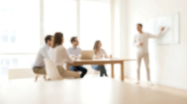 A blurred business meeting shows a man presenting to colleagues seated at a table in a brightly lit modern office setting.
