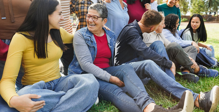 Group of multigenerational people chatting and enjoying time outdoor at city park - Multiracial friends of different ages having fun together - Main focus on left girl face