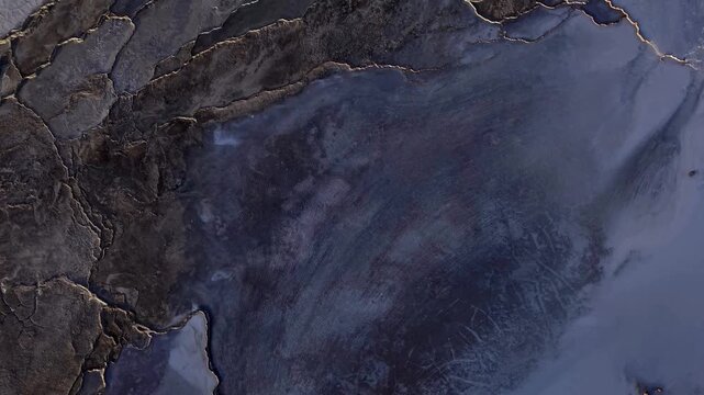 Aerial view of a rugged, cracked landscape with dark rock formations contrasting against lighter, textured surfaces, Grindavikurbaer, Iceland.