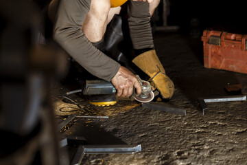 Focused worker grinding metal with angle grinder in dark workshop. Man creating bright spark while cutting steel. Intense concentration during manual labor and craftsmanship