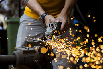 Focused worker grinding metal in workshop. craftsman uses power tool, creating shower of hot...