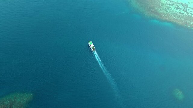 Aerial view of a ferry boat sailing on the turquoise sea, leaving a trail of white foam near coral reefs, Karimunjawa, Central Java, Indonesia.