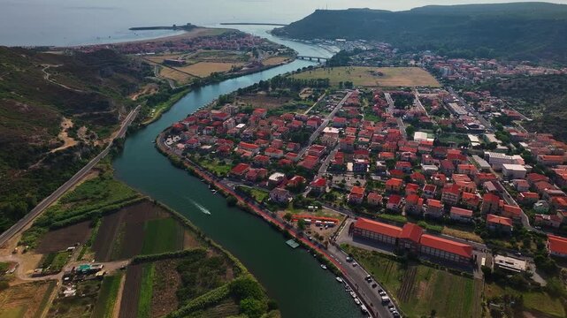 Aerial view of the Temo river flowing into the sea, surrounded by green hills and buildings with red rooftops, Bosa, Sardinia, Italy.