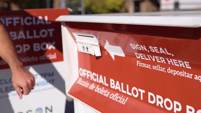 Young Man Places Mail-In Ballot Envelope in Official Voting Drop Box Beside Drop Ballot Here Sign