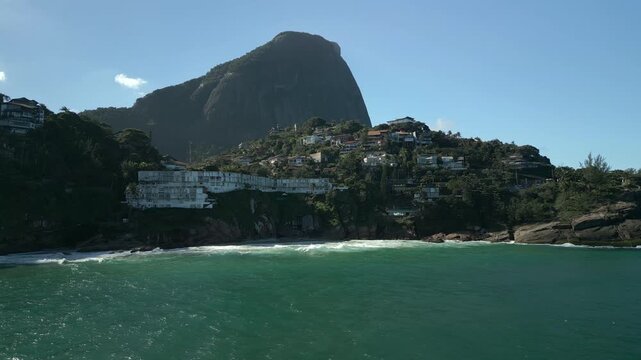 Ocean and luxury houses at Joatinga Beach, Rio de Janeiro. View of cliffside shore mansions and large hills in 4K Apple ProRes 422. Left tracking aerial over the water during morning.