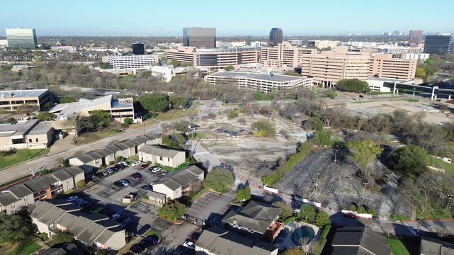 Mixed use expansion view spanning Fair Oaks Ave toward Greenville Ave shows residential rows bordering cleared lot, rising commercial blocks. Roof tones, sparse foliage visual rhythm in Dallas