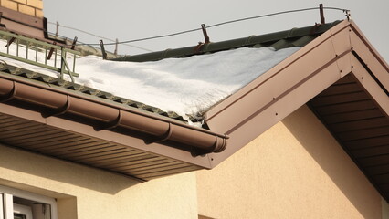Ośnieżony dach domu wielorodzinnego z rynnami oraz ochroną przed ptakami