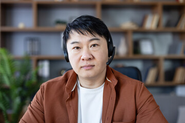 Fototapeta premium Man in headset looking directly at camera, having a video conference call from home office, representing remote work, technical support, or online communication
