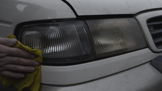 Wiping the front headlight of an old car with a damp cloth to remove dirt and dust