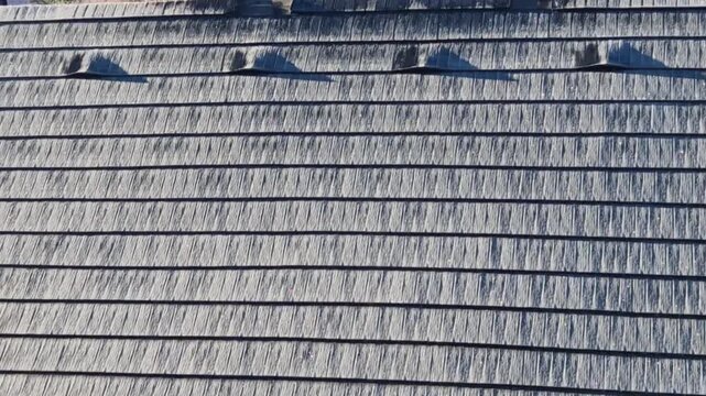roof tiles made of plastic imitation wooden shingles. view of rows of gray narrow recycled boards. vents in several elegant bumps. snow and icicles, asphalt, bitumen, recycled