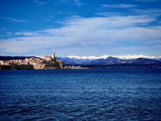 Naklejka premium Antibes,France-Febrary 19,2026:The coastline on the French Riviera in Antibes.View at snow mountains through the sea 