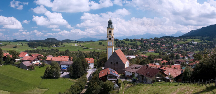 Views of Pfronten with church under blue sky and green hills in summer