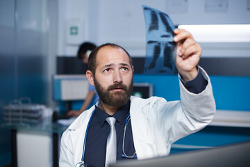 Fototapeta premium Selective focus of a caucasian doctor holding and examining a chest X-ray image of a patient. Close-up shot of a male physician grasping and studying a chest scan of an individual.