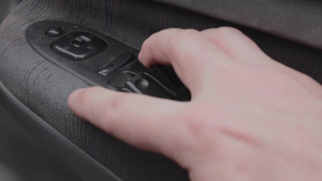 Hand Pressing the Power Window Switch on a Car Door Panel, Close-Up