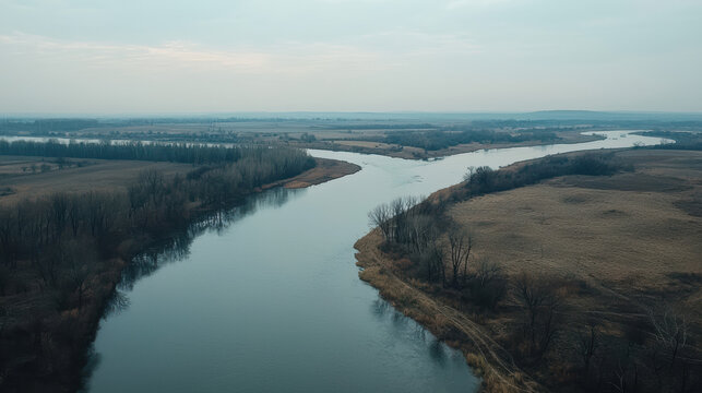 A tranquil aerial view reveals a serene river winding through an expansive landscape of fields and trees under a cloudy sky, showcasing nature's beauty.