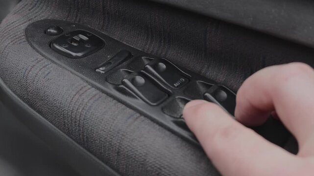 Hand Pressing the Power Window Switch on a Car Door Panel, Close-Up