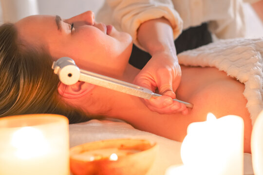 Tuning fork sound therapy with candles, practitioner applying vibration to woman's neck, holistic wellness ritual, relaxation, alternative spa treatment, close up.