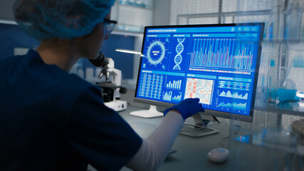 Female scientist in protective clothes and glasses looking at the computer screen. Researching genetic diseases and DNA test results © Marcin Janiec