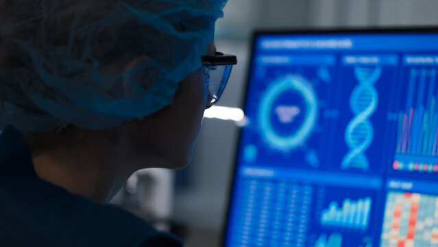 Female scientist in protective clothes and glasses looking at the computer screen. Researching human genetic diseases and DNA test results