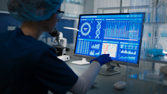 Female scientist in protective clothes and glasses looking at the computer screen. Researching genetic diseases and DNA test results