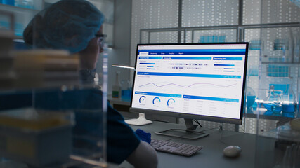 Female scientist in protective clothes and glasses looking at the computer screen. Researching diseases and test results © Marcin Janiec