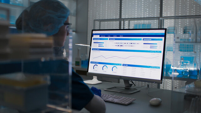 Female scientist in protective clothes and glasses looking at the computer screen. Researching diseases and test results