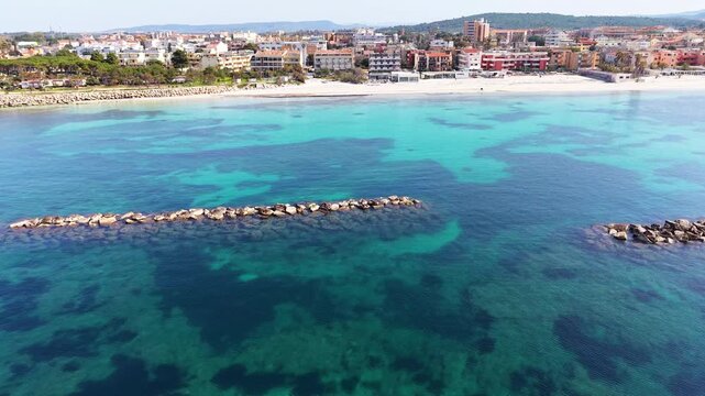 Aerial view of breakwaters along the shore of Alghero in Sardinia during springtime with clear turquoise sea and coastal landscape