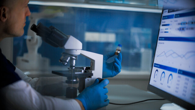 Research work in a medical lab.Man sitting in front of a computer screen and a microscope