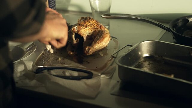 Person seasoning a cooked chicken with a seasoning blend in a kitchen.