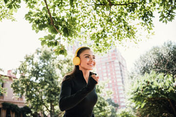 Outdoor fitness woman enjoys sunny day in the park wearing headphones and activewear while training...