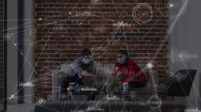 Applications icons connecting with lines, graphs over coworkers in masks discussing over laptop