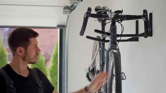 Man lifting bicycle on wall mounted rack in garage. Concept of bike storage, home organization and cycling equipment care