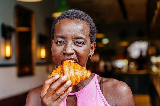 Playful Black woman biting croissant in close up cafe portrait