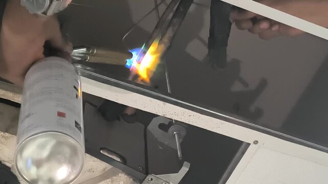 HVAC technician using gas torch for brazing copper pipe of split air conditioner indoor unit during installation service.
