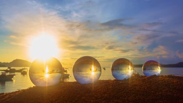   Time lapse of a golden sunset reflected in four crystal spheres resting on the beach. Each glass orb mirrors the glowing sky, calm waves, and soft sand, creating a surreal and tranquil scene.