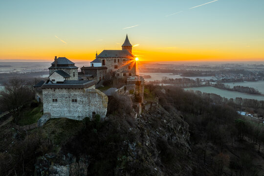 Aerial Drone Shot of Historic Kuneticka Hora Castle Silhouetted Against a Vibrant Sunrise Sky, Enveloped in Winter Morning Mist Over the castle and Surrounding Countryside, Pardubice Region, Kunětick&aacute;