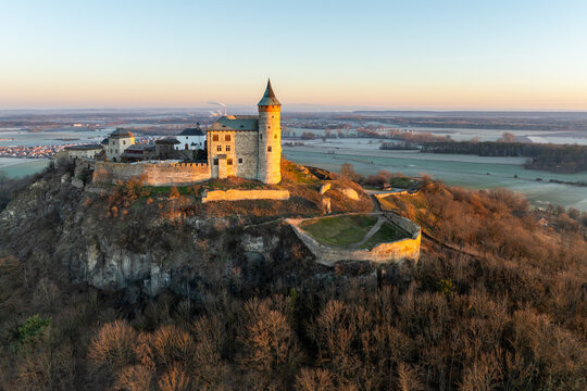 Aerial Drone Shot of Historic Kuneticka Hora Castle Silhouetted Against a Vibrant Sunrise Sky, Enveloped in Winter Morning Mist Over the castle and Surrounding Countryside, Pardubice Region, Kunětick&aacute;