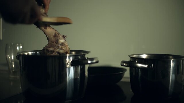 Person stirring a pot of food with a wooden spoon, surrounded by three other pots and a glass on a dark kitchen countertop.