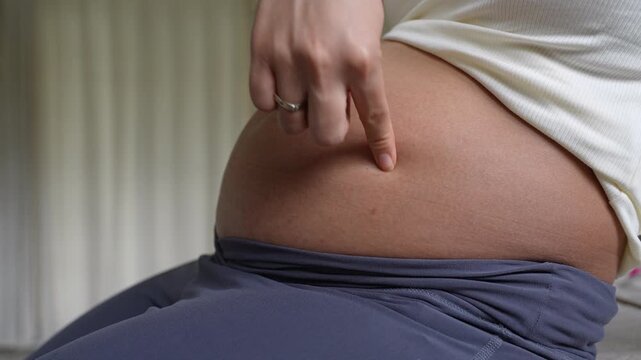 Close-up of pregnant woman tenderly tracing her baby bump with her finger