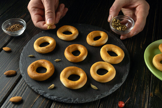 Baker prepares snacks or baranka with hands and spices on table in kitchen during daytime.