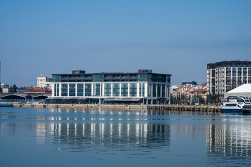 Obraz premium a modern white hotel or commercial building located on a waterfront pier, reflecting in the calm, still water under a clear blue sky.