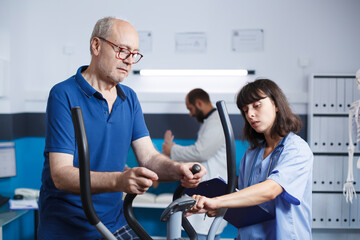 Senior male patient doing physical exercise for injury recovery with help from female nurse....