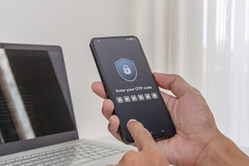 Fototapeta premium Two factor authentication OTP code for secure login. A man using a laptop and smartphone to log in by entering One Time Password code.