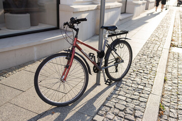 Obraz premium red bicycle is parked on a city street paved with pavement tiles on a sunny day. Move around the city on a comfortable, environmentally friendly transport